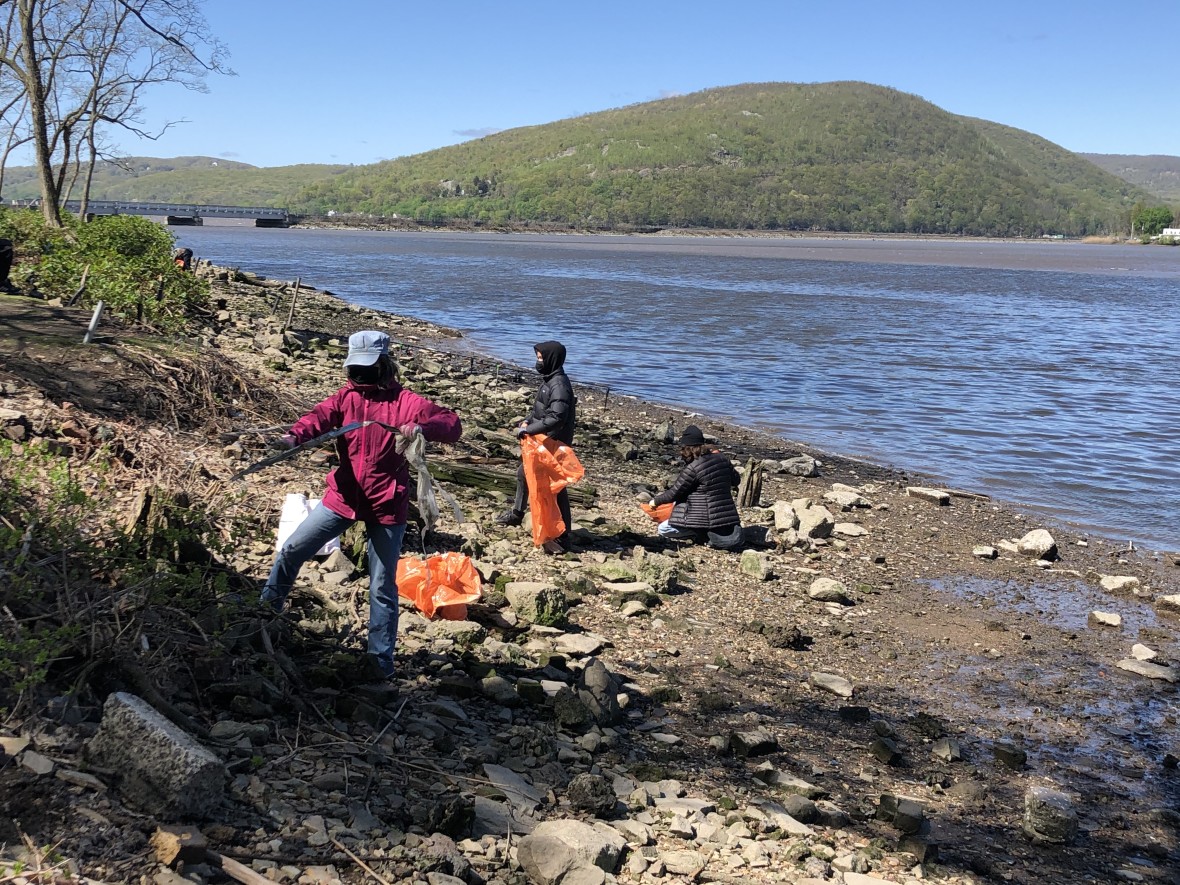 Three volunteers cleaning up debris on the rocky shore of the Hudson River