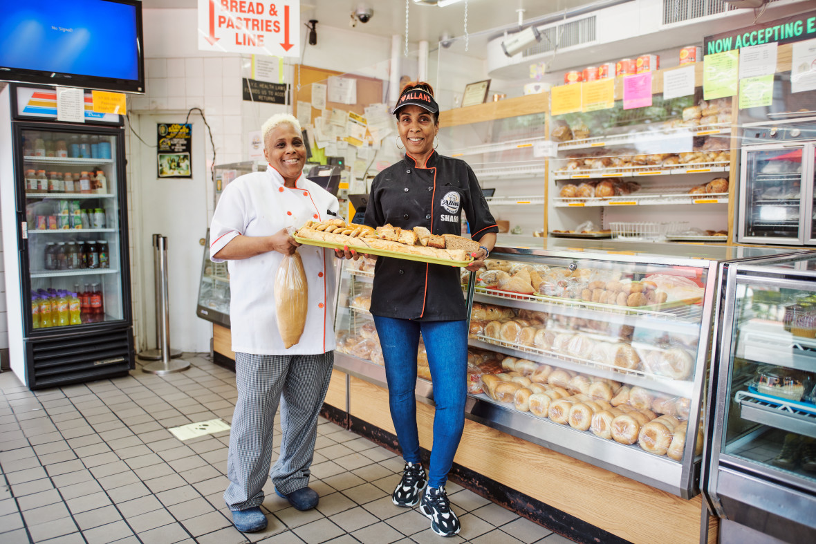 Two Allan's Bakery employees holding a tray of baked goods while standing in front of bakery case