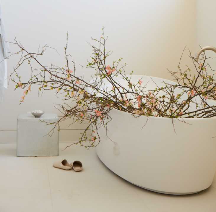 Interior of a spa treatment room with float tub filled with branches with pink flowers at the Shou Sugi Ban House in Water Mill