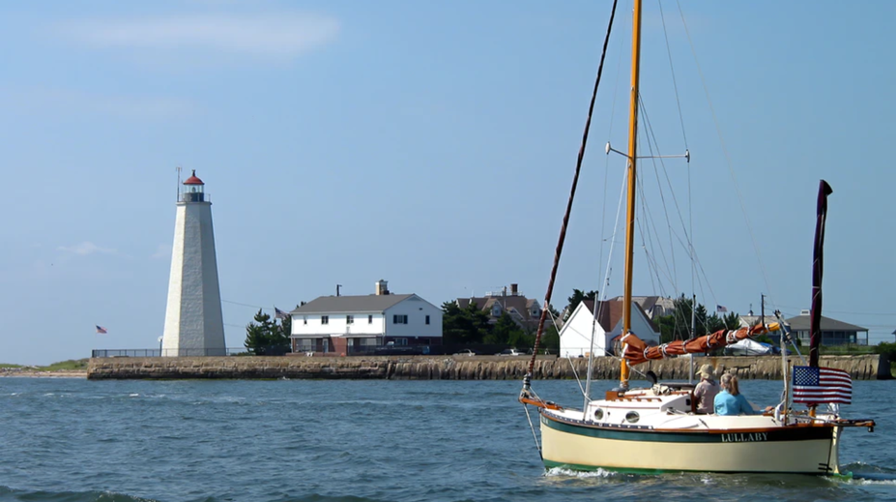 Sailboat sailing on water towards lighthouse on penisula