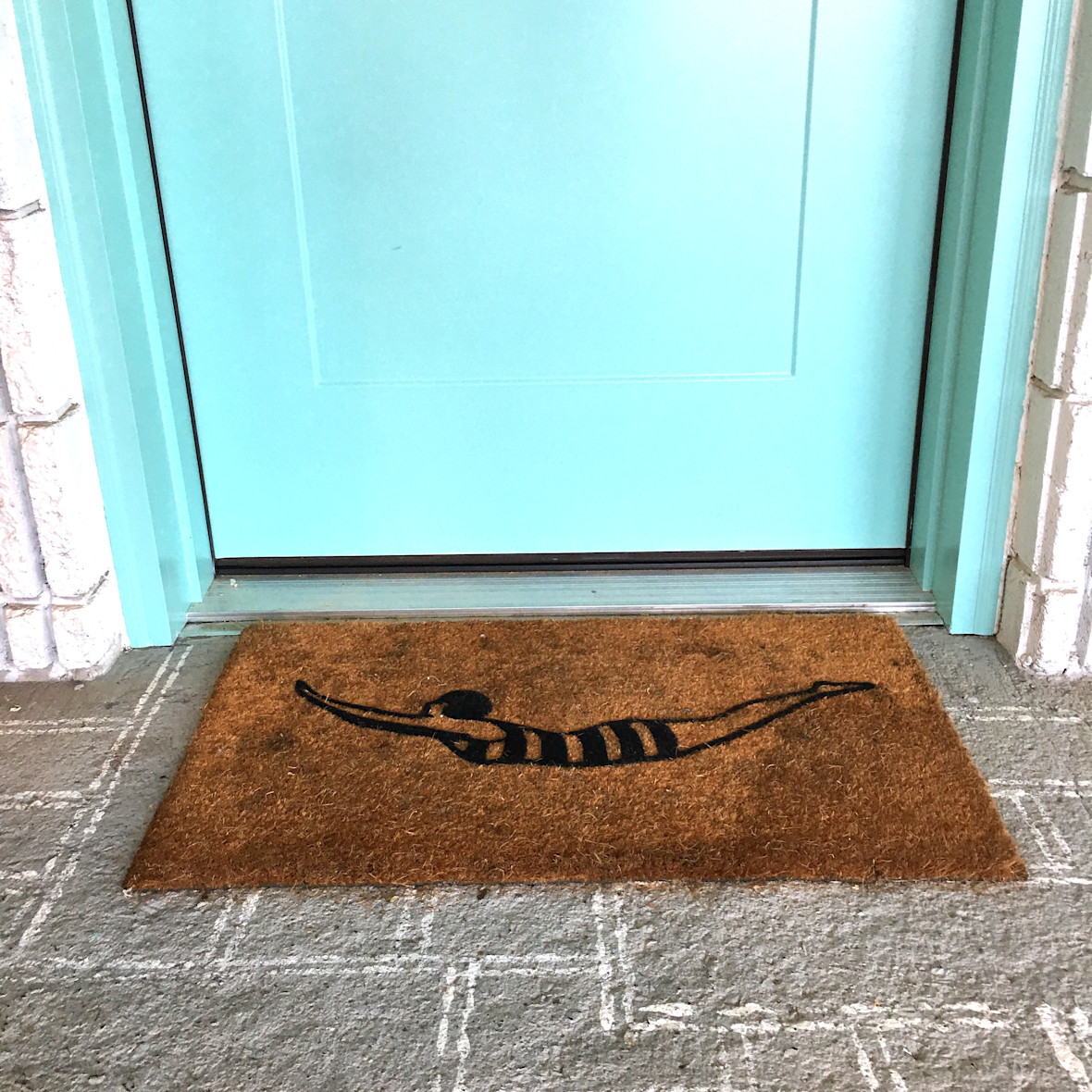 Welcome mat with diver on it at base of teal door