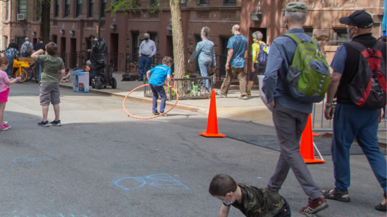 Child draws with chalk on open NYC street while two individuals walk by at Car Free Earth Day 2021
