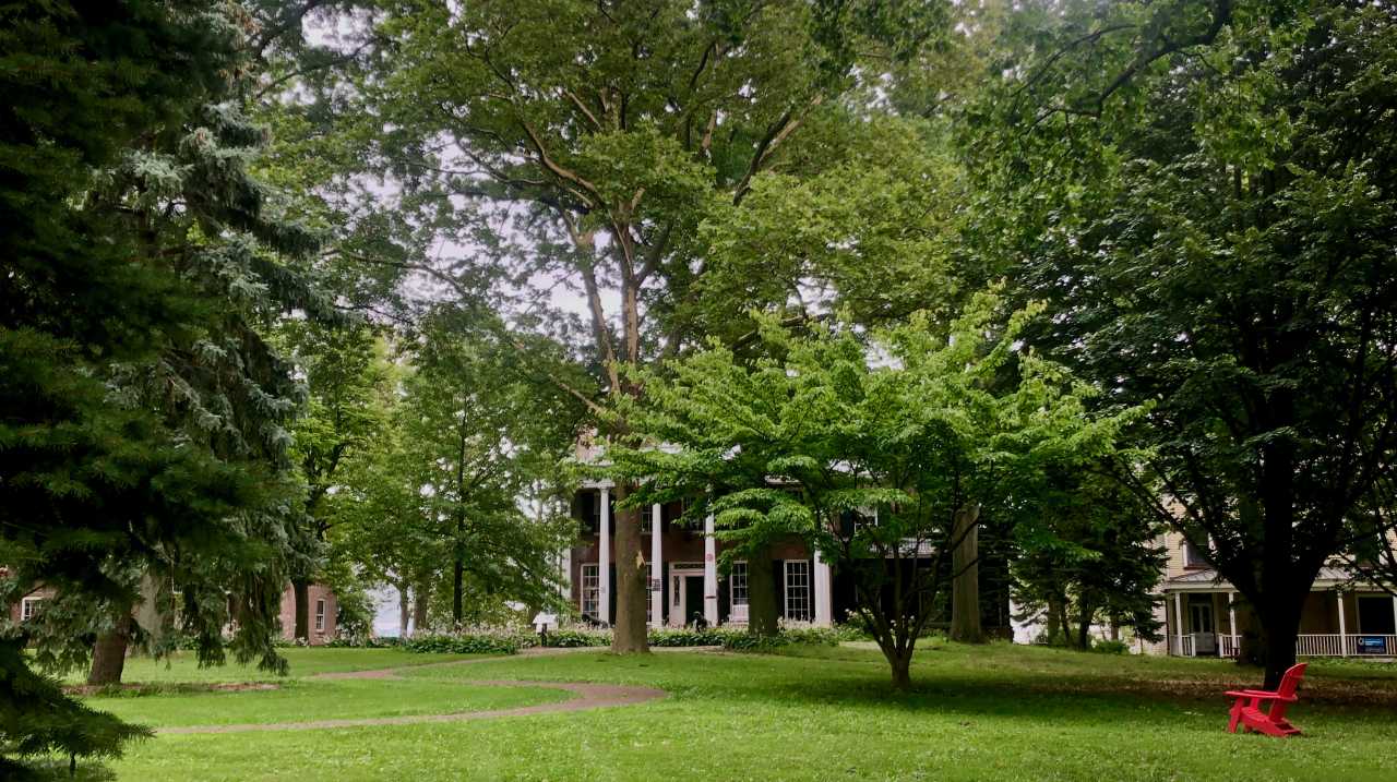 Historical brick buildings surrounded by trees with green lawn in foreground