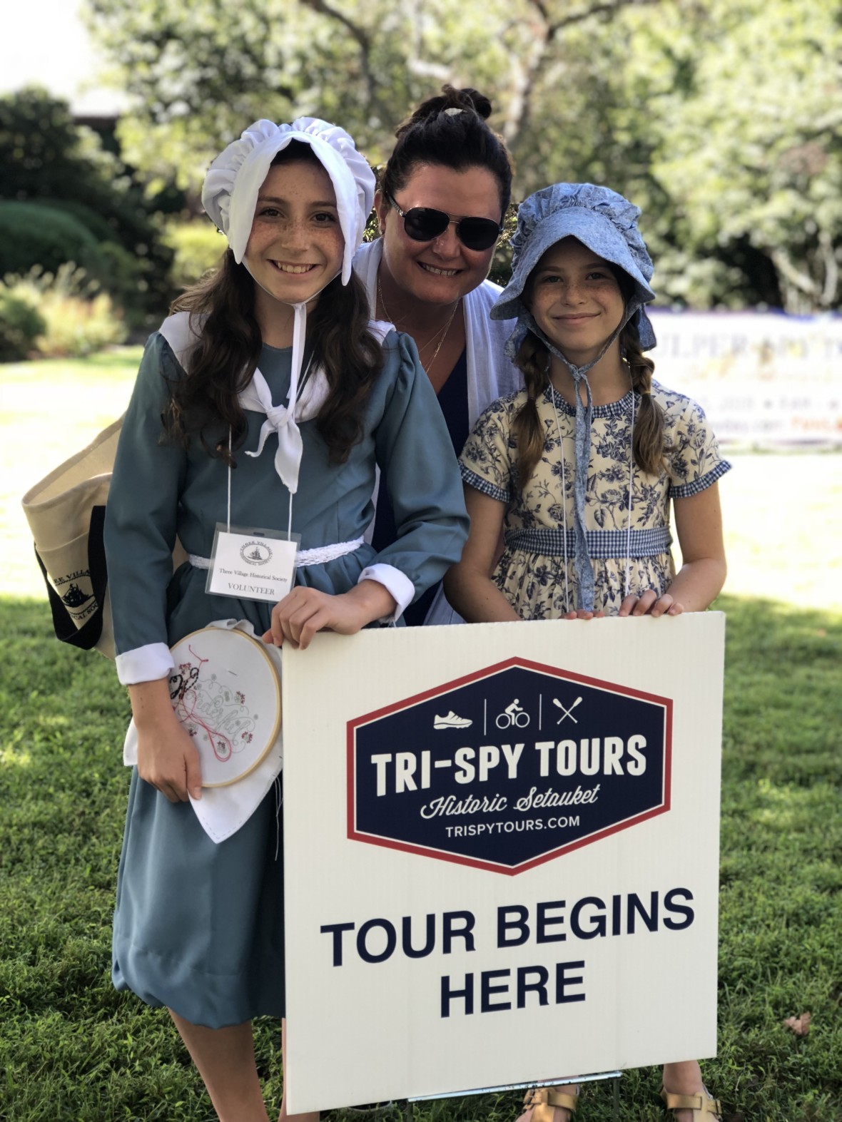 An adult and two young children in colonial garb pose in front of the Tri-Spy Tours sign