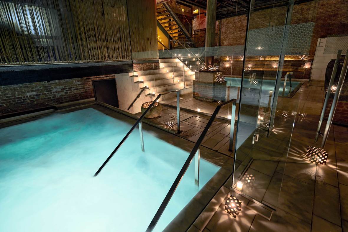 Interior of Aire Ancient Baths in Manhattan with low, decorative lighting and staircases into small, teal soaking pools