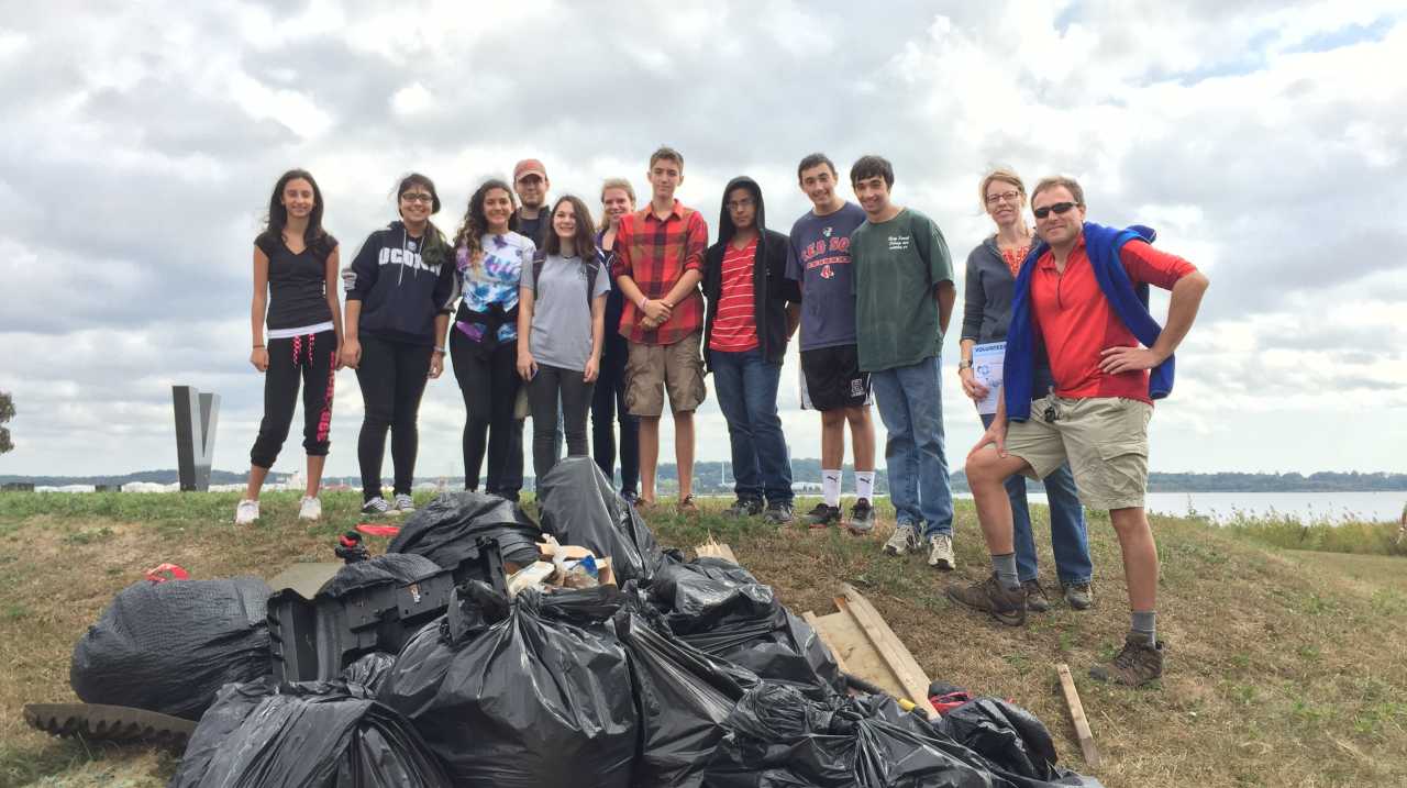 Members of Connecticut Cleanup standing atop a hill with a pile of full black garbage bags