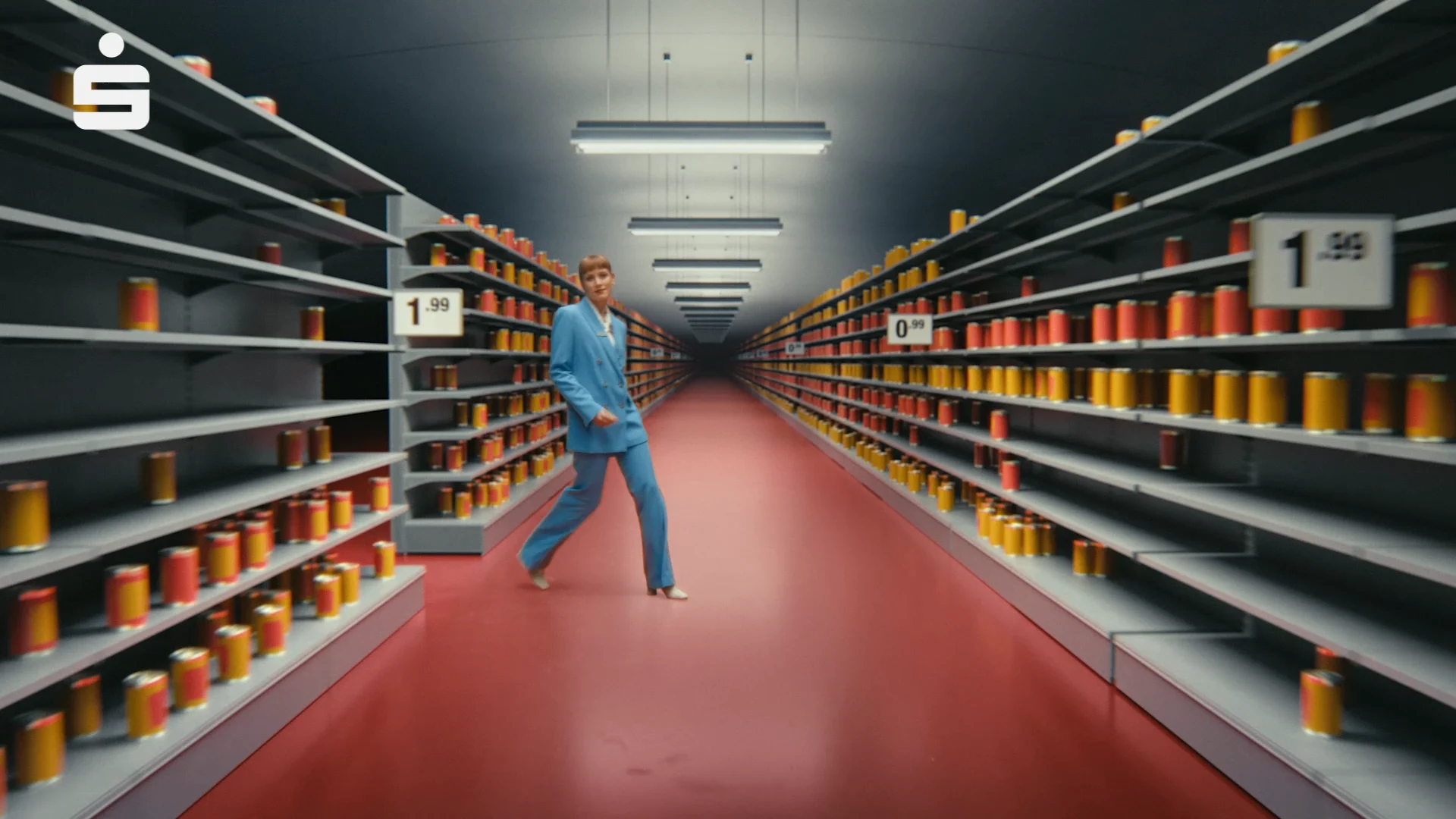 a woman walking between two shelves in a super markes. in both shelves there are red and orange cans and price tags