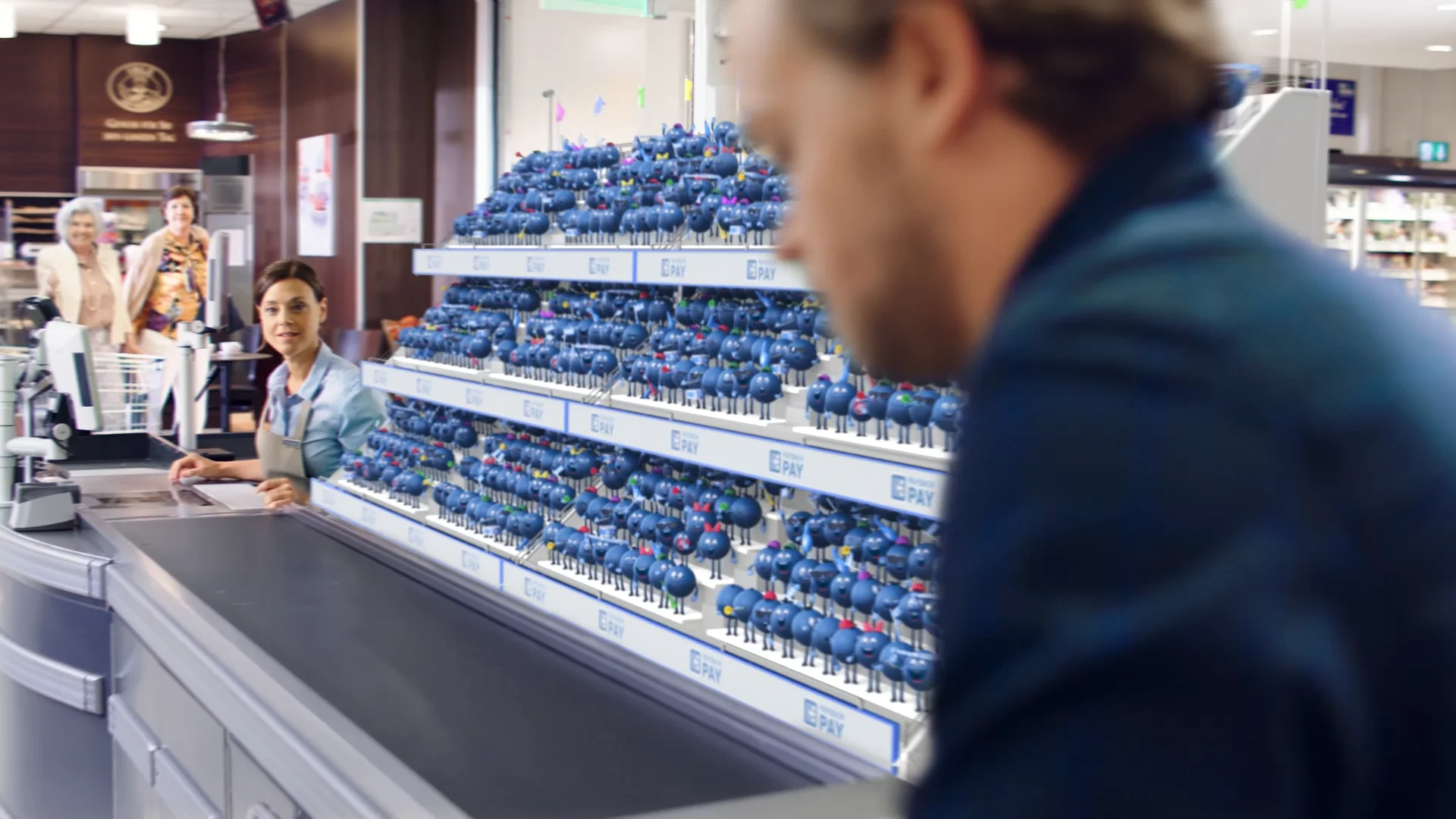 a man in a supermarket in front of a grandstand filled up with litte blue payback point 3d characters who are cheering at him
