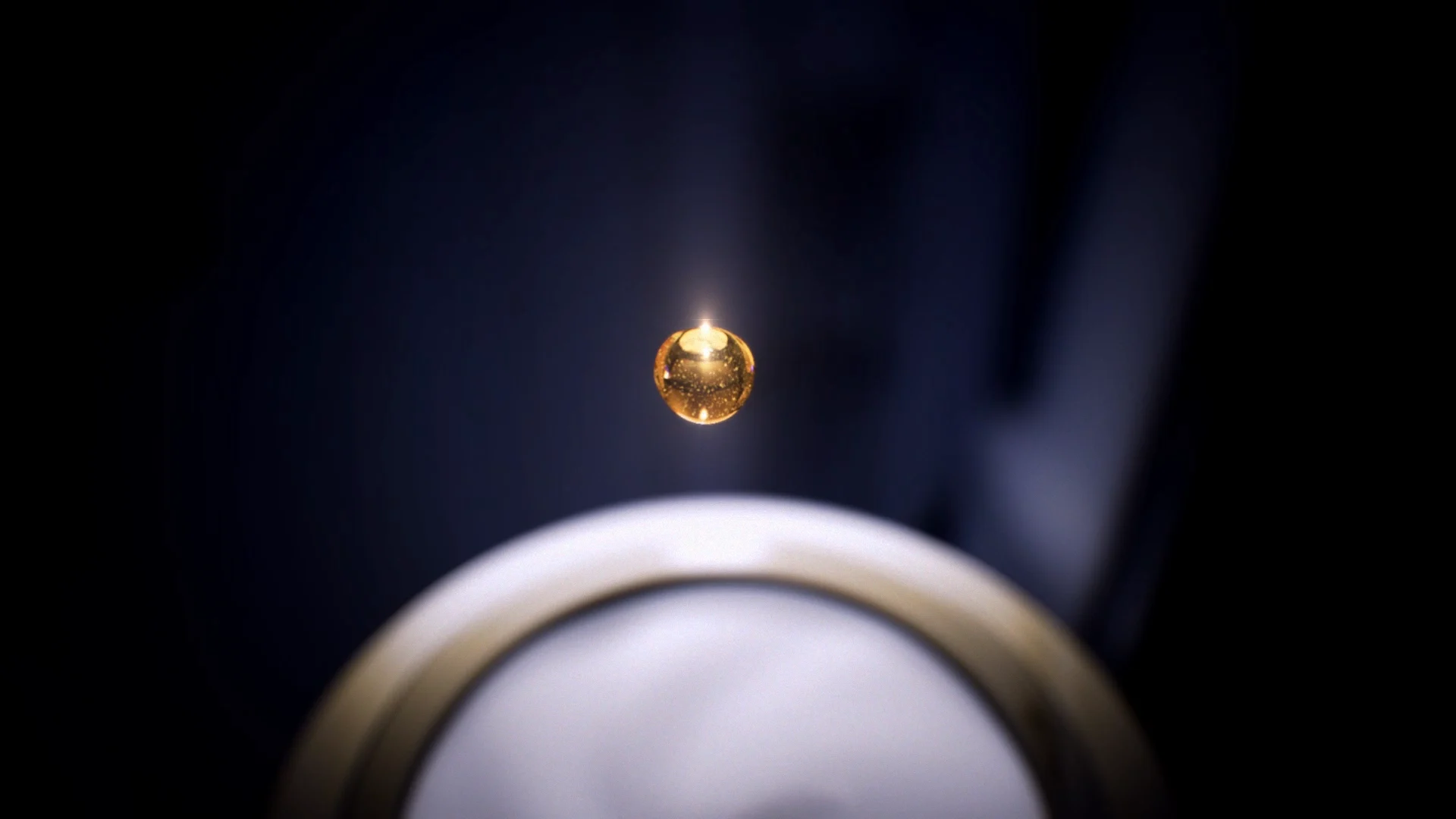 a golden drop in front of a black background falling into something white golden which is not recongnizable