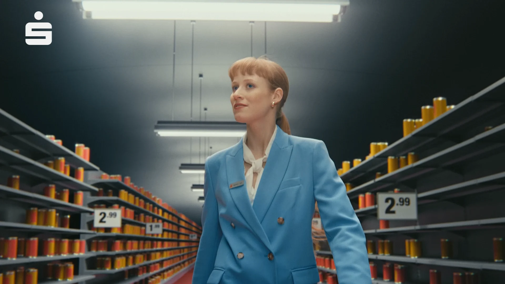 a woman walking between two shelves in a super markes. in both shelves there are red and orange cans and price tags