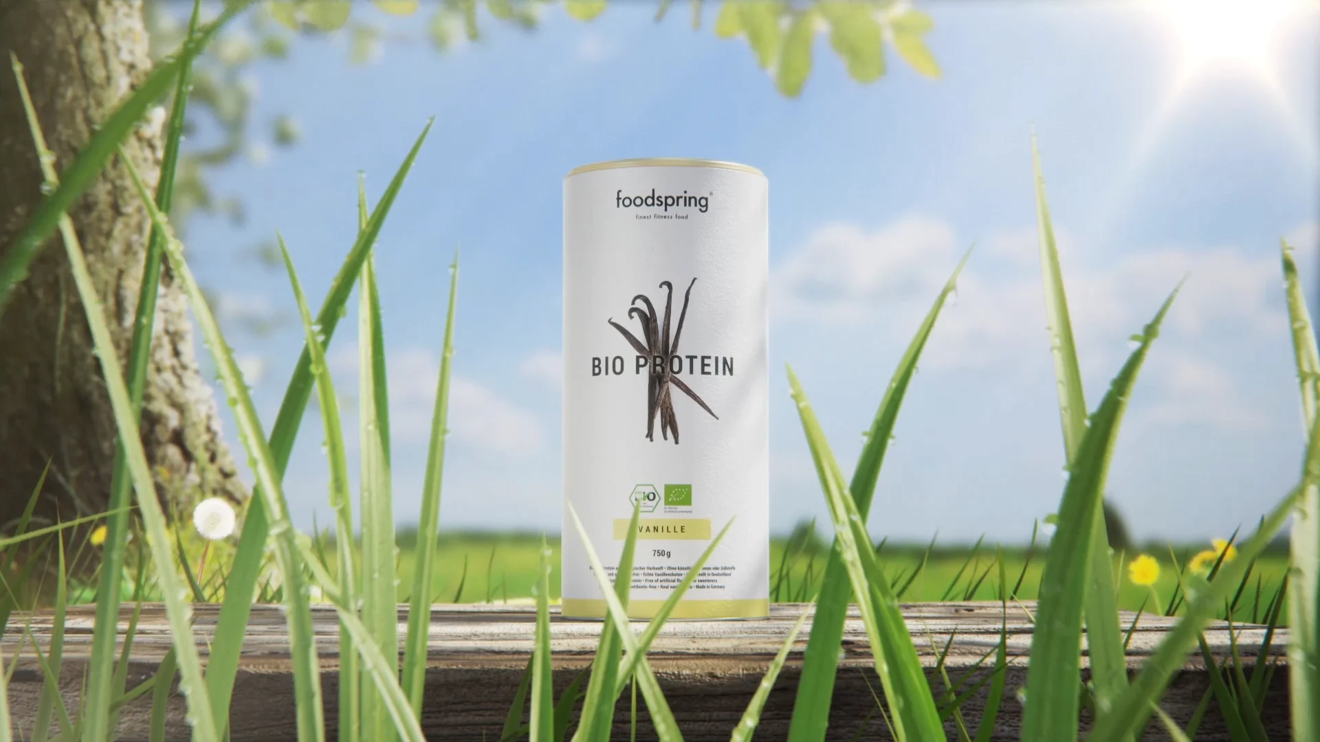 a foodspring bio protein packshot on a table in front of a tree and a field under blue sunny sky. 