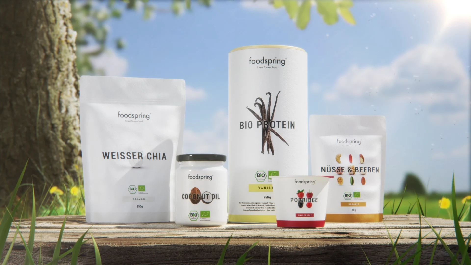 a range of foodspring protein shake packshots standing on a table in from of a tree and a field