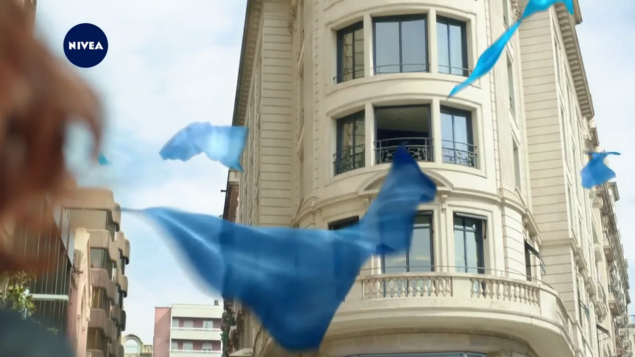 a woman looking up to a building where several blue silk scarfs are flying around