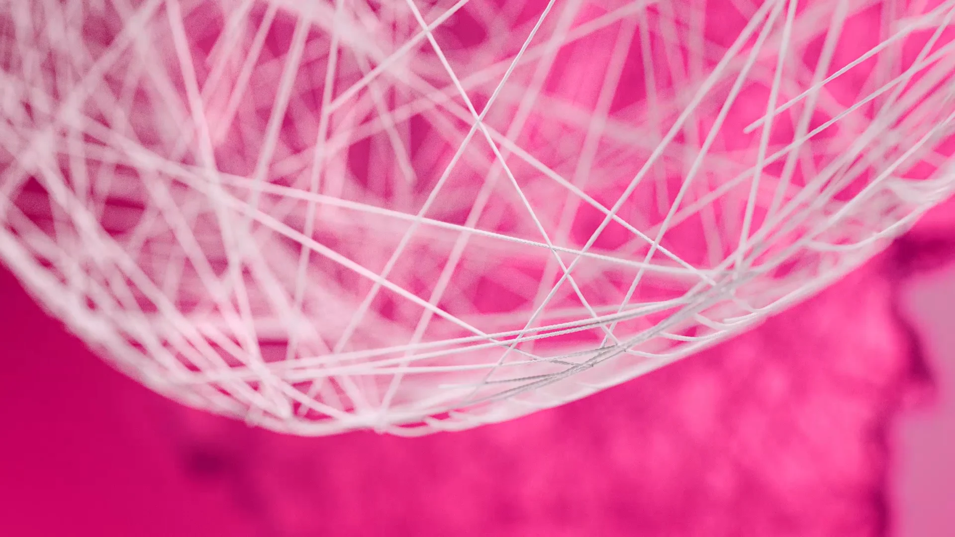 close up of a net weaved out of white strings in front of an abstract magenta background