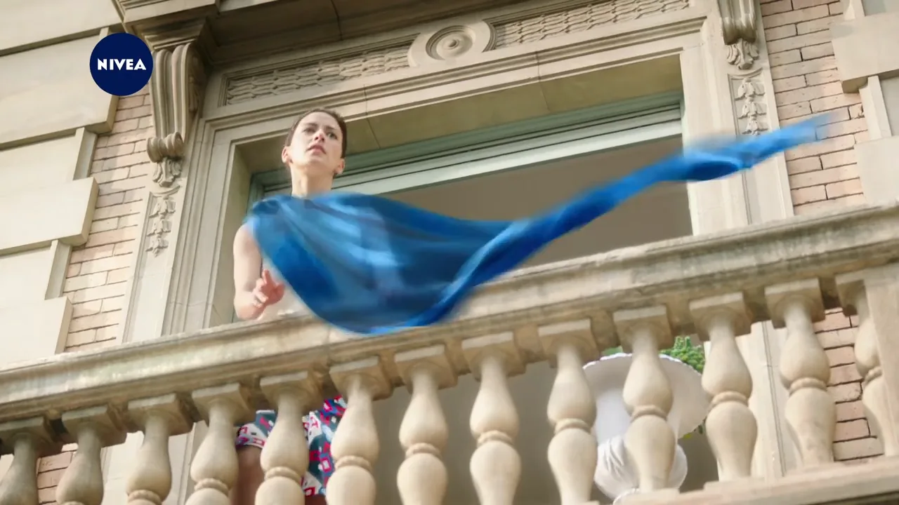 a woman at the bannister of a balcony of an old building trying to catch a  blue silk scarf
