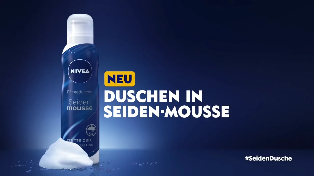 a nivea Seiden-Mousse packshot in front of a blue background. The pack is white-blue and is standing behing a little dip of foam