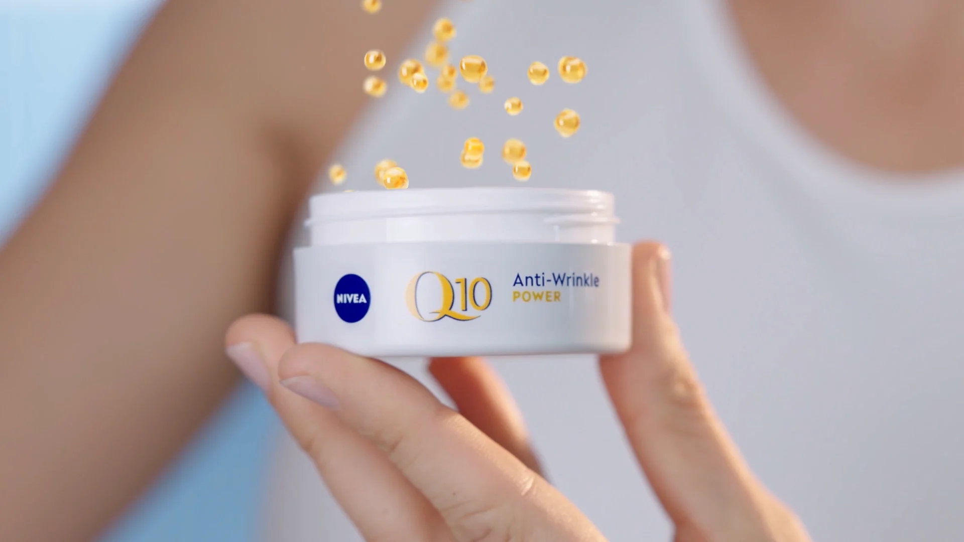 yellow bubbles falling into a white Nivea Q10 anti wrinkle packshot which is been hold in a hand. woman blurred in the background