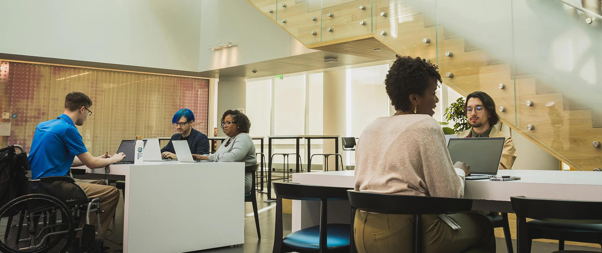 Several male and female employees work collaboratively together on their laptops at an open-concept work station.