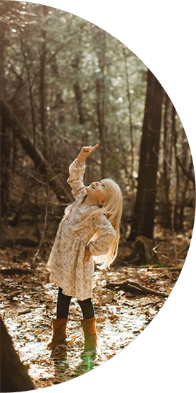 Girl in the woods pointing up at the trees