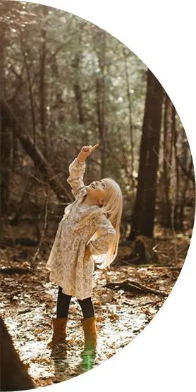 Girl in the woods pointing up at the trees
