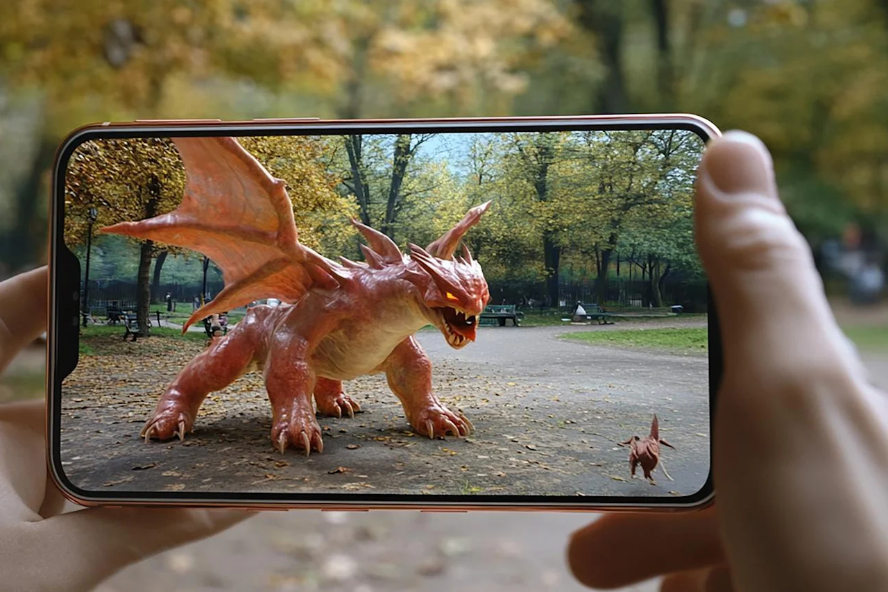 A phone pointing at a park with an image of the park on the screen with a dragon added to the image.