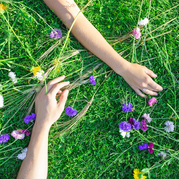 Hænder på græs med blomster strøet omkring