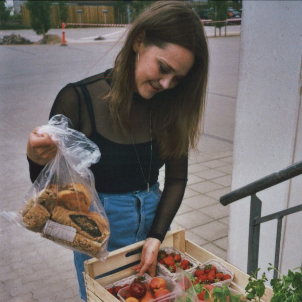 Iben Østergaard Fog står med en kasse med overskudsgrøntog en pose brød