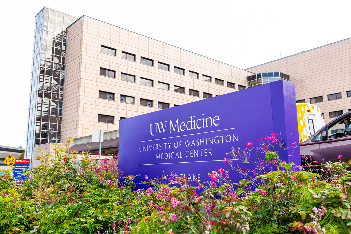 A purple sign for the University of Washington Medical Center sits among flowers outside UWMC. 