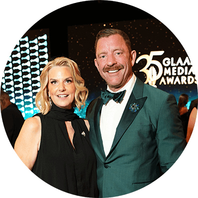 Brent Miller stands in a green tuxedo jacket beside GLAAD President and CEO Kate Ellis, who wears a black evening gown. Behind them, the words 35 GLAAD Media Awards are displayed onstage.
