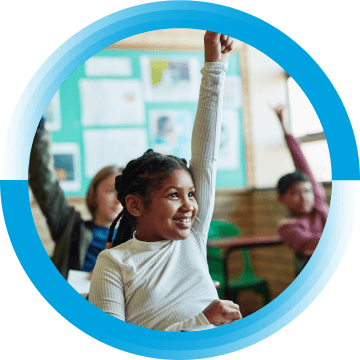 A young girl is raising her hand in a classroom. There are two other students behind her raising their hands.