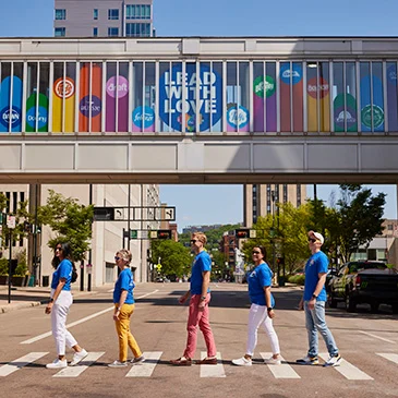 Five P&G employees crossing a cross wallk with rainbow bridge and brand logos in the background