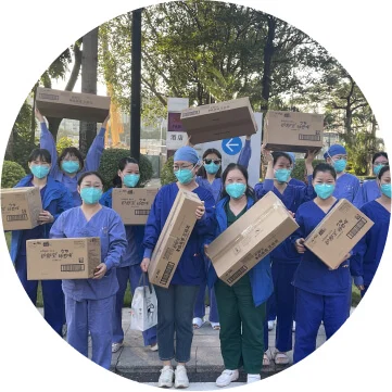 A group of ten people in blue scrubs and medical face masks are holding cardboard boxes with the P&G logo on them.