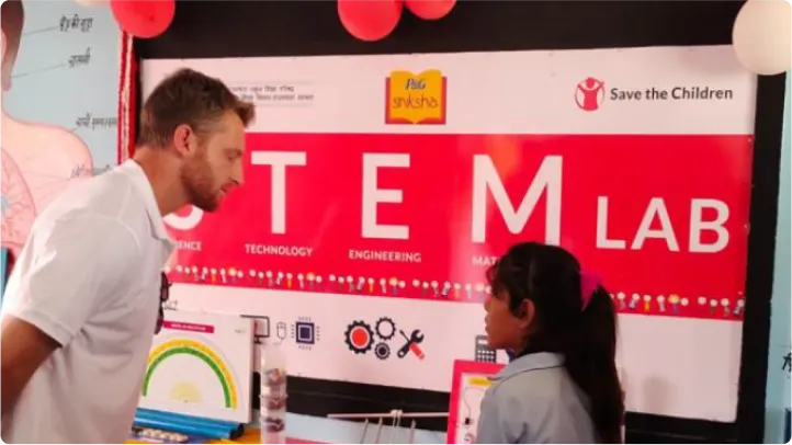 A man and young girl are standing in front of a “STEM Lab” poster facing each other.