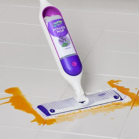 A purple and white Swiffer PowerMop device cleans up an orange liquid on a tiled floor.