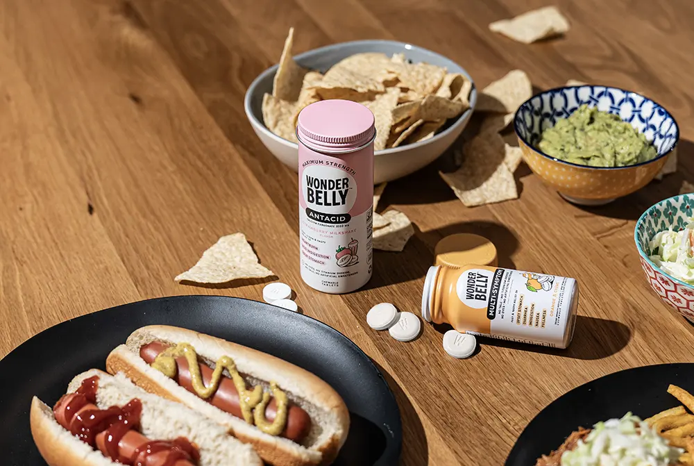 Two Wonderbelly antacid containers on a wooden table with food on it.