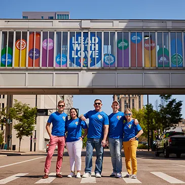 Five members of P&G’s GABLE employee resource group stand in front of a bridge with a sign that reads, “Lead with Love.”