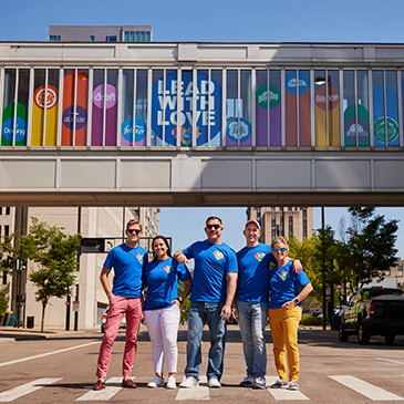 Five members of P&G’s GABLE employee resource group stand in front of a bridge with a sign that reads, “Lead with Love.”