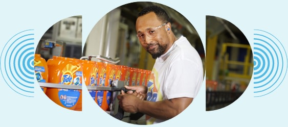 A man wearing safety glasses smiles as he monitors Tide Pods on a conveyor belt