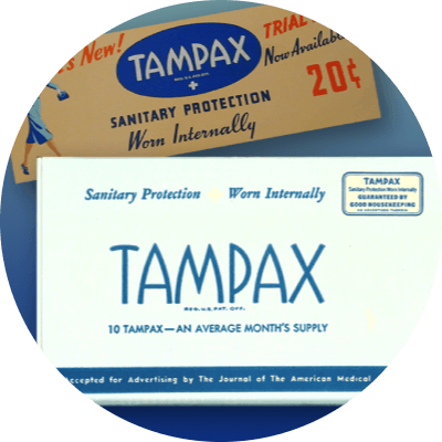 A white box top with blue text displays "Tampax." Another brown box top includes colored text and an illustration of a woman in a blue skirt suit. Both boxes are historical versions of Tampax packaging. A full page magazine clip sits on the right.