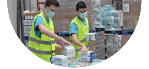 Two men wearing masks and high-visibility safety vests handle P&G products inside a warehouse