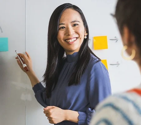 Man and woman writing on whiteboard while another woman looks on, her back to the camera.  