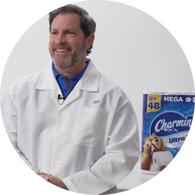 A man with short light brown hair in a white lab coat. Next to him is a blue and white plastic package of charmin toilet paper.