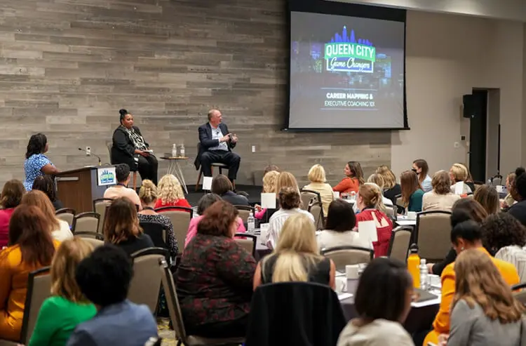 Monica Turner, President - North America of Procter & Gamble, and Jon Moeller, Chairman, President and CEO of Procter & Gamble, sit onstage addressing a conference room of women.