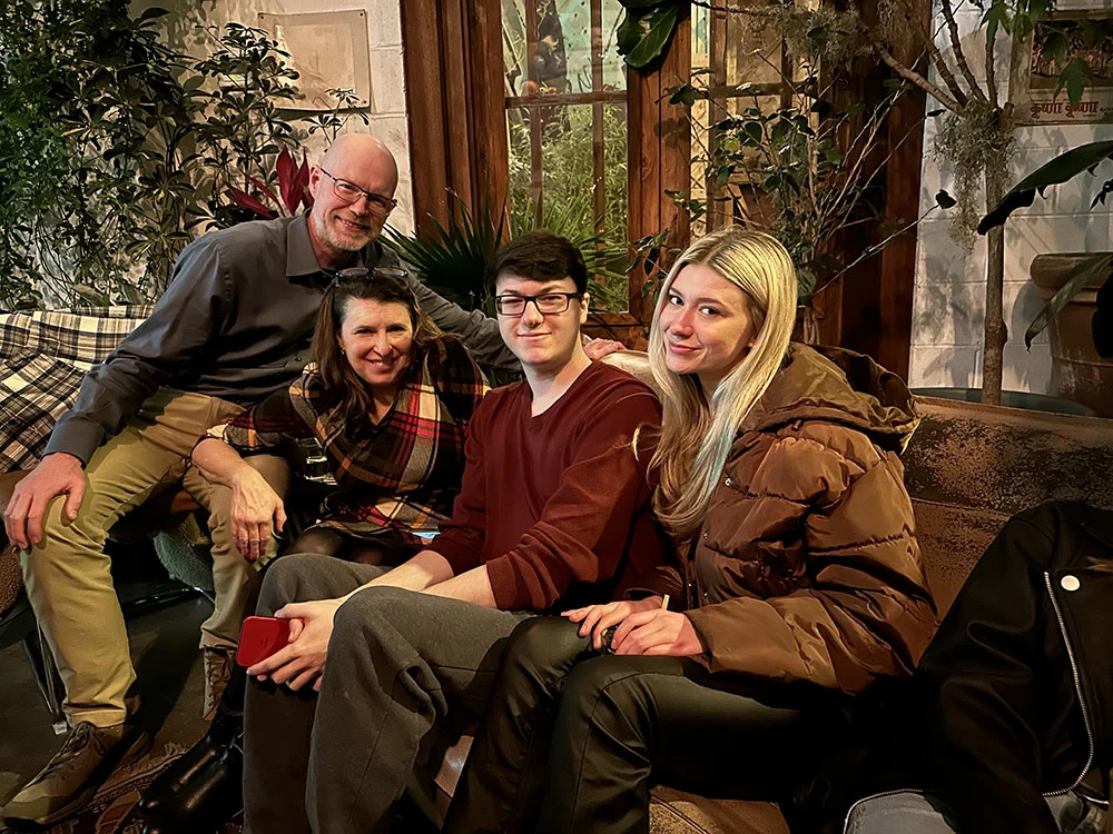 An adult female, an adult male and a young boy and girl sit together on a couch as they smile at the camera.