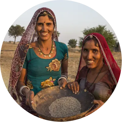 Two women wearing head coverings smile and hold a metal basin