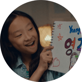 A young Asian girl smiles as she holds up a sign with the American and Korean spellings of her name.