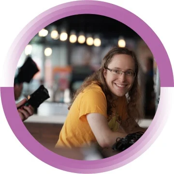 A woman in glasses and a yellow shirt is smiling towards the camera.