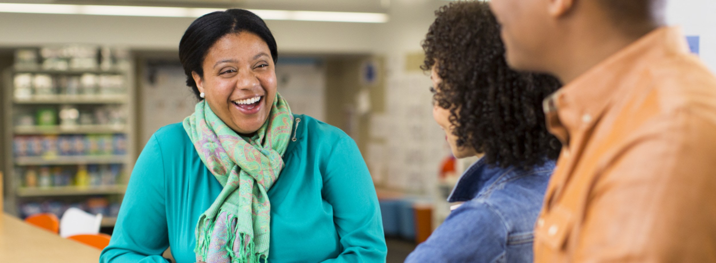 Smiling woman speaks with two colleagues whose backs are to the camera. 