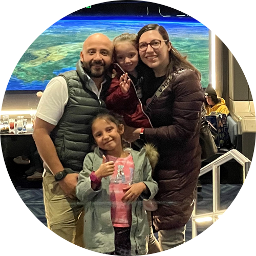 An adult woman, adult man, and two young girls pose together in the Space 220 Restaurant at the Walt Disney World Resort. The restaurant windows simulate a panoramic view of Earth from outer space.