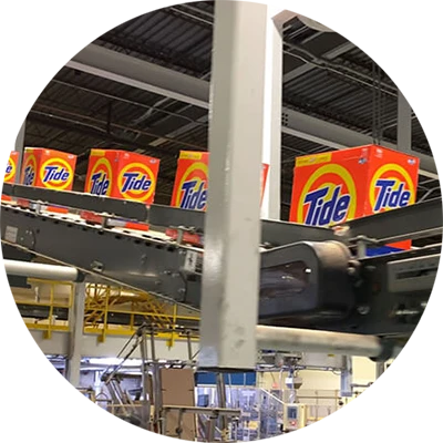 Boxed laundry detergent moves along on a production line above manufacturing equipment in a manufacturing plant.